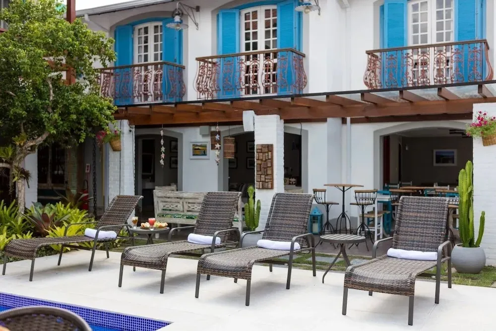 Transats et tables basses disposés devant une maison blanche à balcons bleus.