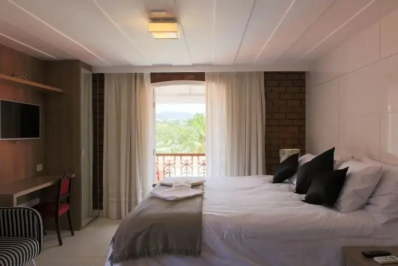 Une chambre lumineuse avec un lit double et un balcon ouvert sur un paysage verdoyant.