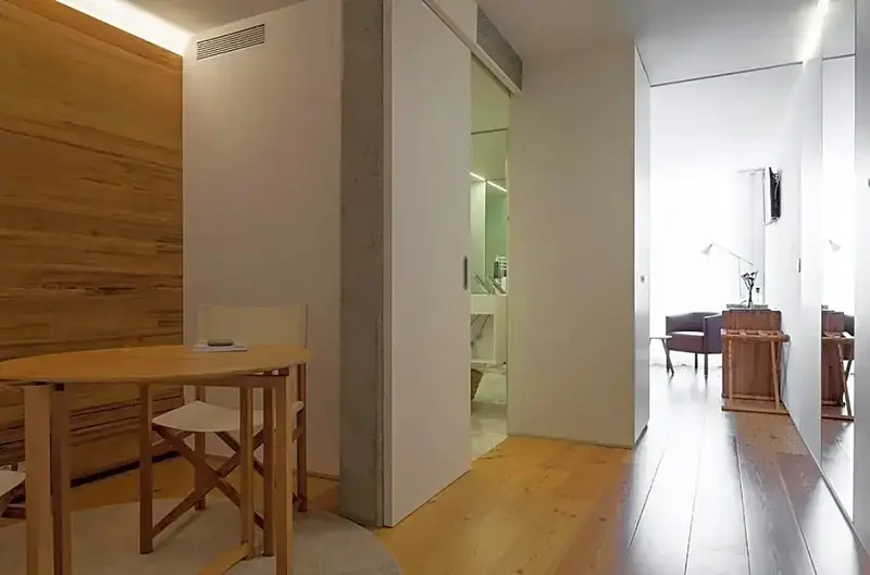 Une table ronde et des chaises se trouvent dans un espace lumineux avec un parquet clair.