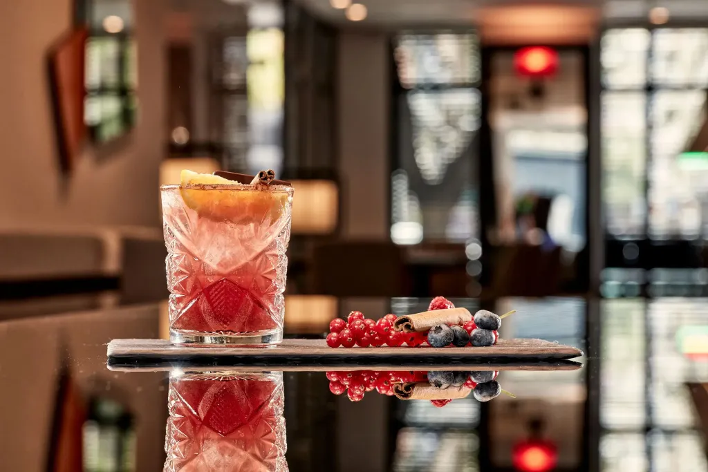 Un cocktail coloré est présenté sur une planche en bois avec des fruits rouges et des baies.