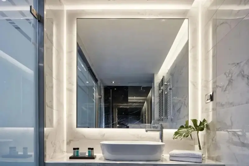 Une salle de bain moderne avec un grand miroir lumineux et un vasque blanche.