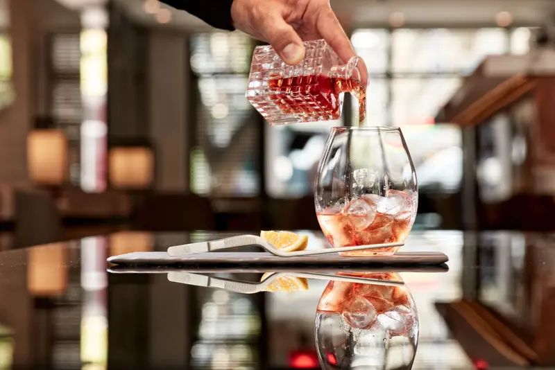 Un cocktail est versé dans un verre rempli de glaçons et d'une tranche d'orange.