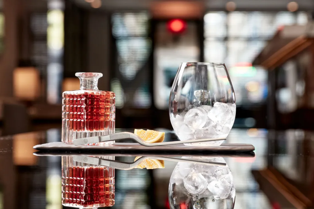 Un verre et une bouteille de liquide ambré reposent sur un plateau noir brillant.