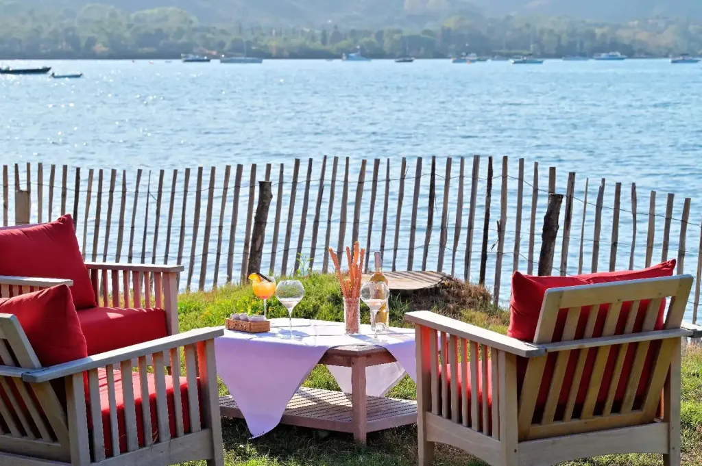 Deux fauteuils rouges et une table basse avec des boissons sont disposés face à la mer.