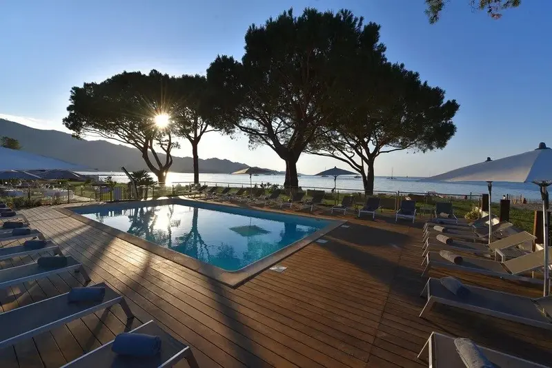 Une piscine bordée de chaises longues au soleil couchant.