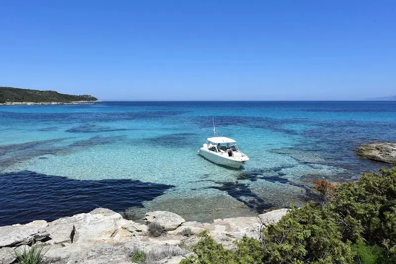 Un bateau de plaisance navigue dans une eau turquoise peu profonde près d'une côte rocheuse.