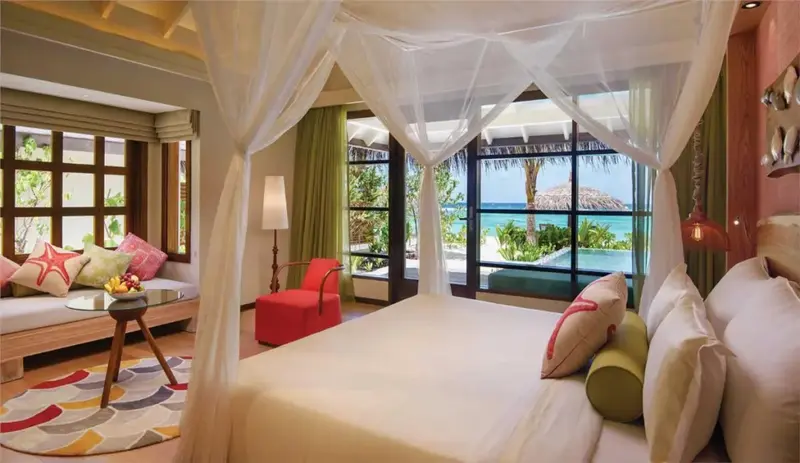 Une chambre lumineuse avec un lit à baldaquin donnant sur une piscine et la mer.