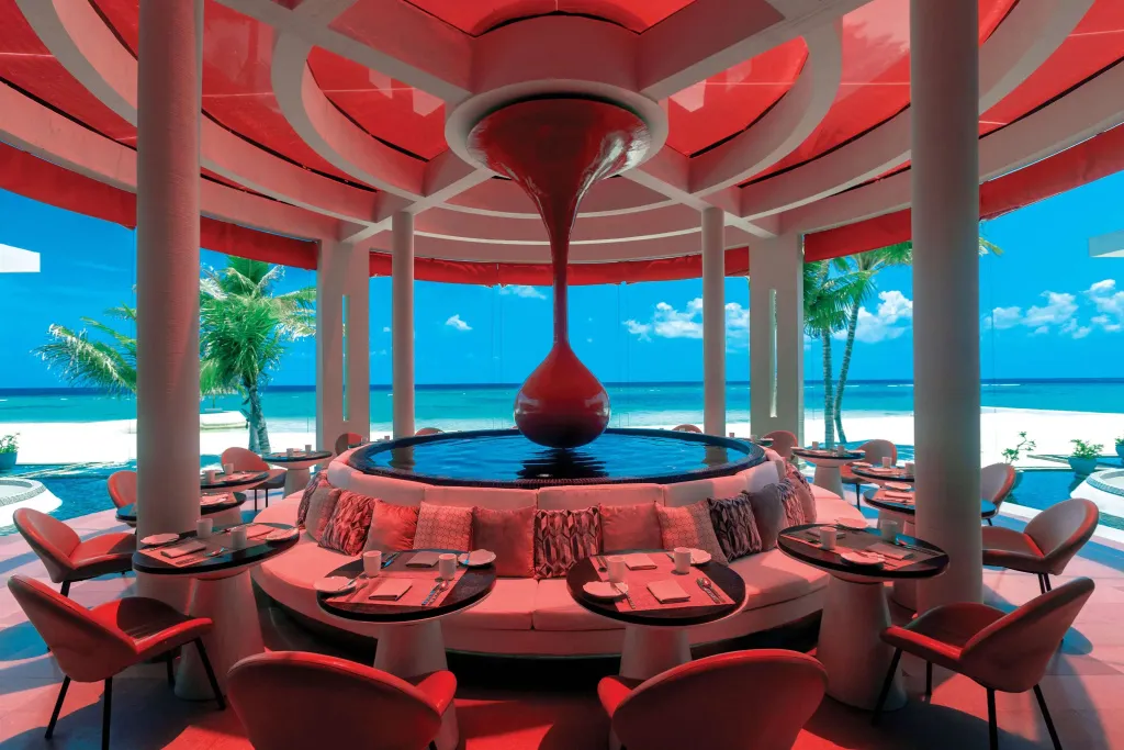 Un restaurant circulaire rouge offre une vue sur la mer turquoise et une plage de sable blanc.