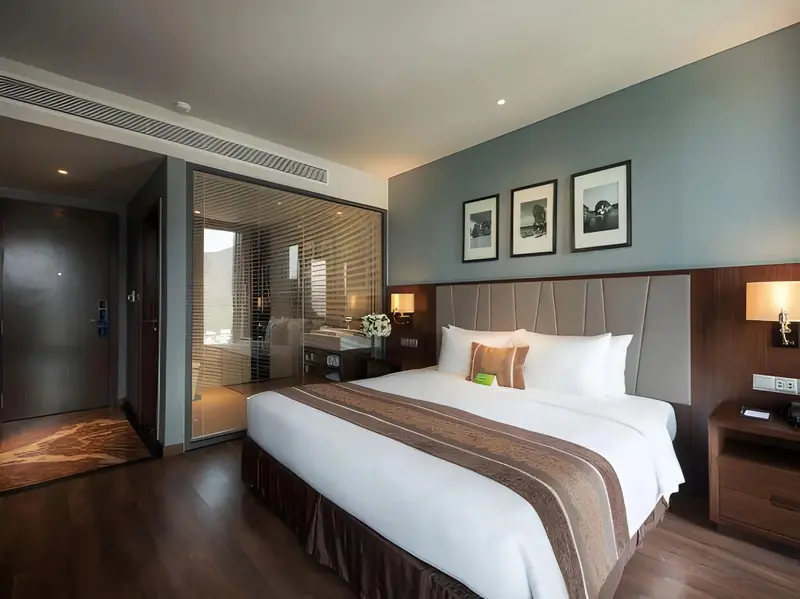 Une chambre lumineuse avec un grand lit et un espace salle de bain visible à travers une paroi vitrée.