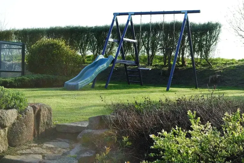 Une balançoire et un toboggan se dressent sur une pelouse verdoyante.