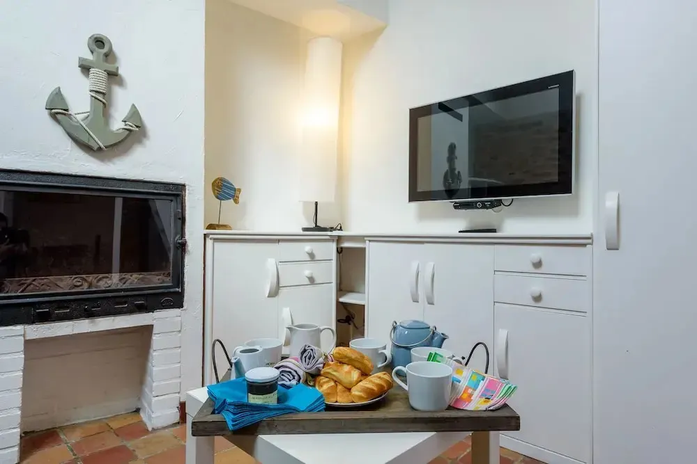 Une table basse présente un petit déjeuner avec des viennoiseries et des boissons chaudes devant un téléviseur et une cheminée.