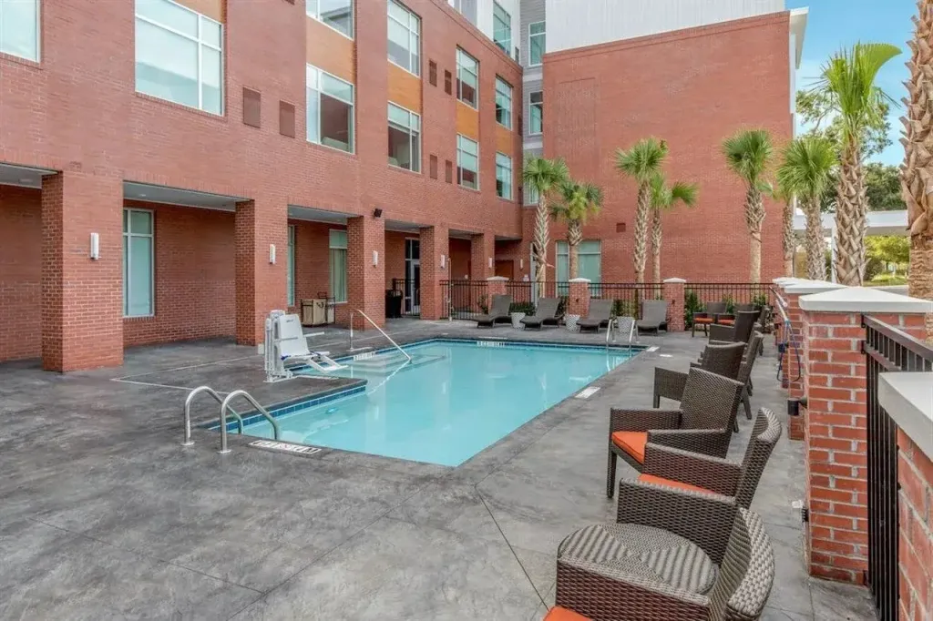 Une piscine rectangulaire est entourée de chaises longues et de palmiers dans une cour intérieure.