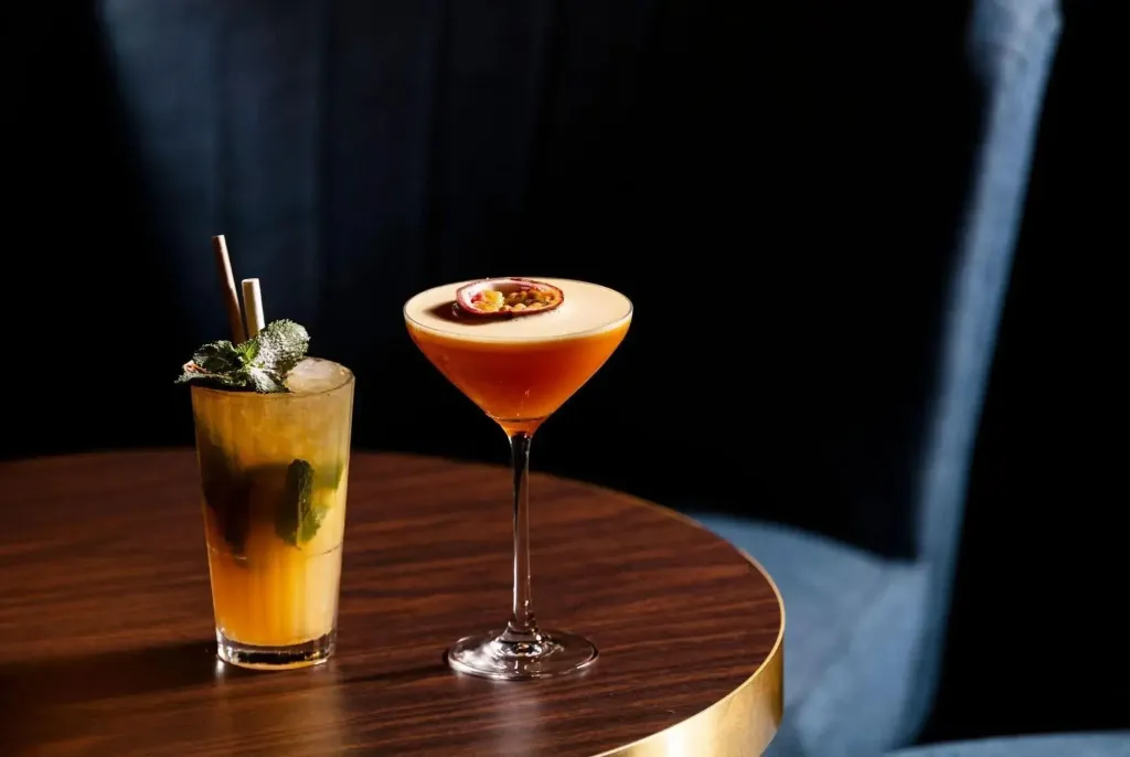 Deux cocktails colorés sont présentés sur une table ronde en bois.