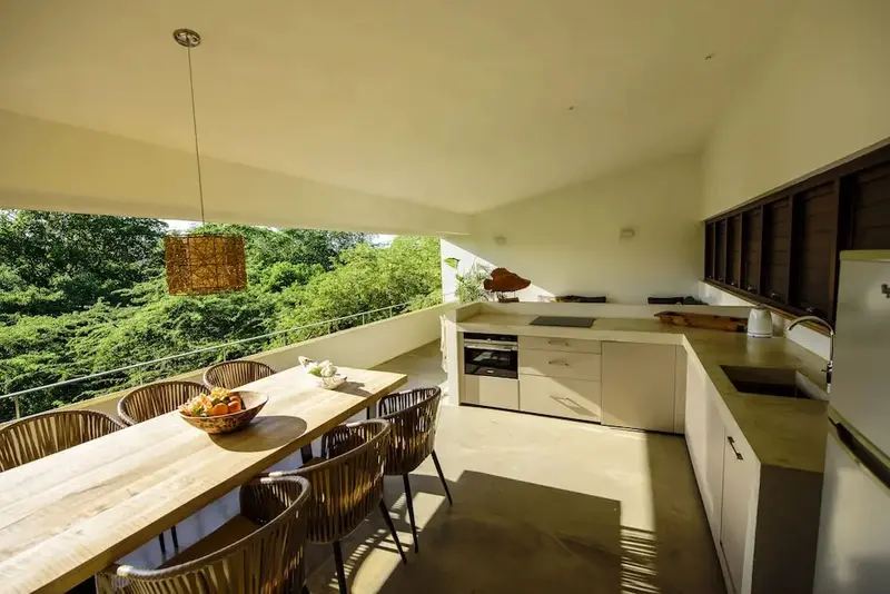 Une table à manger en bois est placée devant une cuisine moderne et lumineuse.