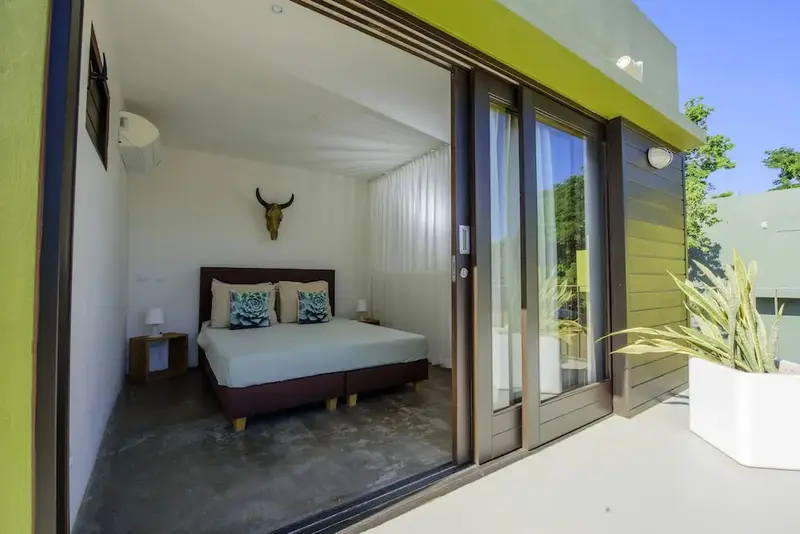 Une chambre lumineuse s'ouvre sur une terrasse avec végétation.