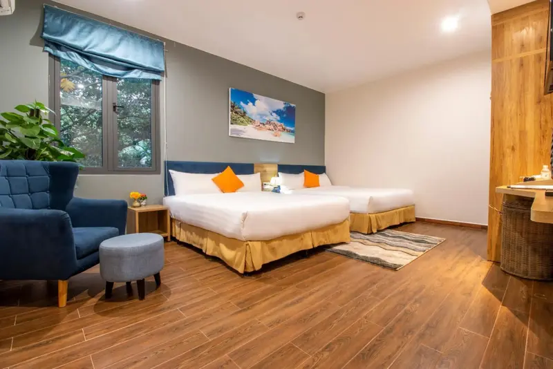 Chambre lumineuse avec deux lits et un coin salon près d'une fenêtre.