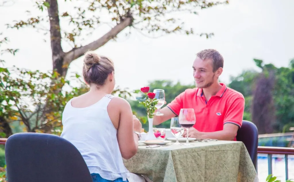 Un couple déjeune à une table en extérieur, avec des verres de vin et des roses.