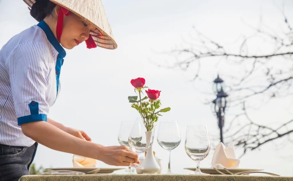 Une personne dresse une table avec des verres et des roses rouges.