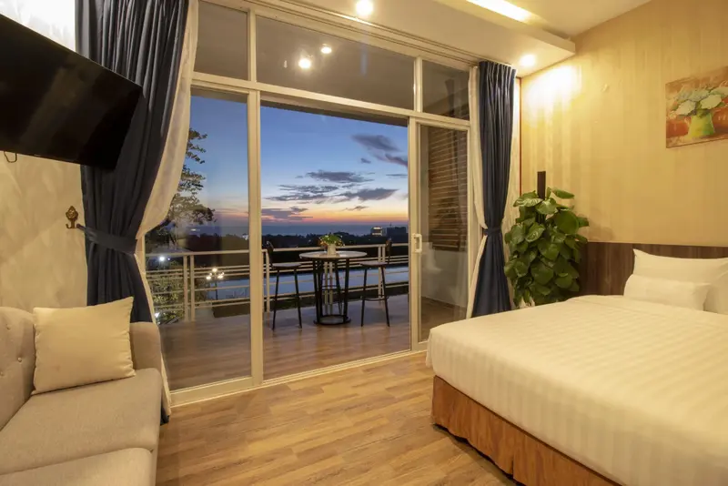 Une chambre lumineuse s'ouvre sur une terrasse avec vue sur un paysage au coucher du soleil.