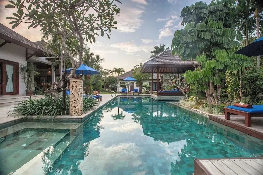 Une piscine turquoise bordée de végétation luxuriante et de transats bleus.