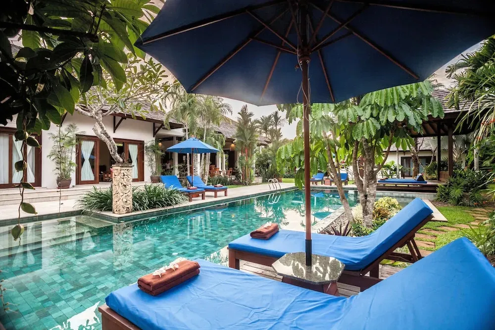 Transats bleus disposés autour d'une piscine turquoise dans un jardin tropical.