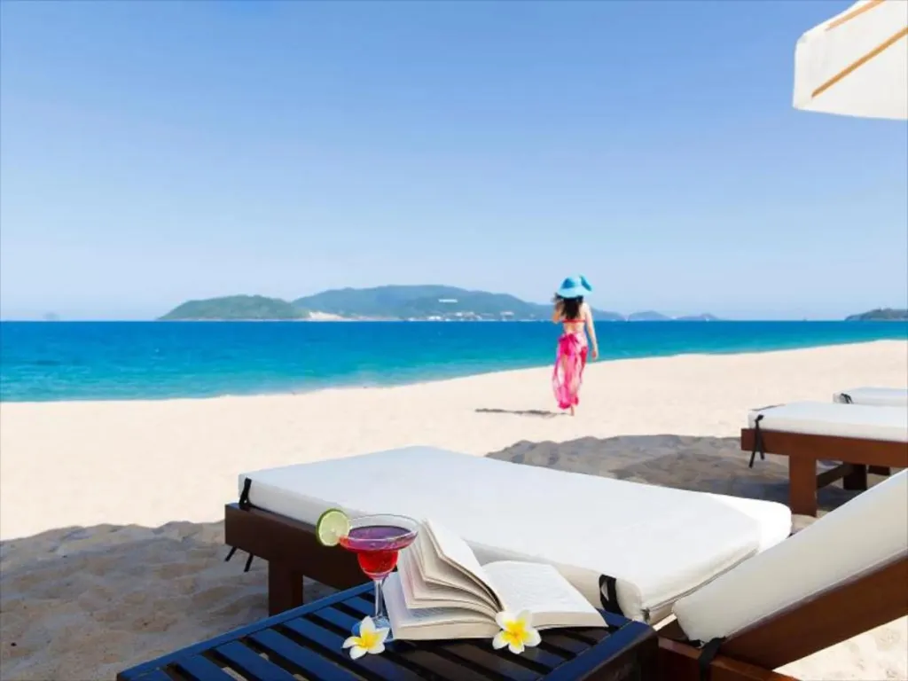 Transats sur une plage de sable blanc avec un cocktail et un livre.