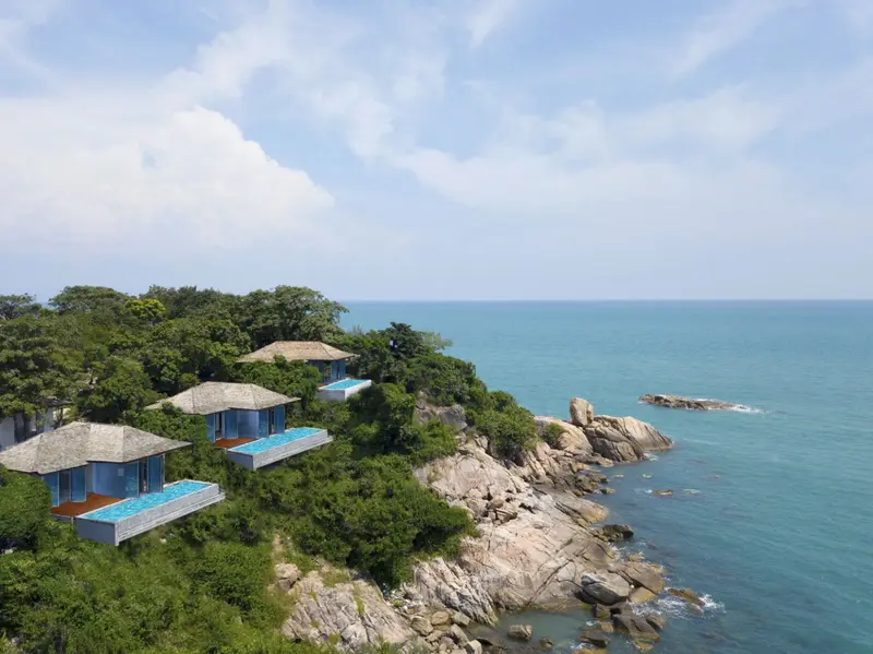 Des bungalows avec piscine surplombent une côte rocheuse et la mer.
