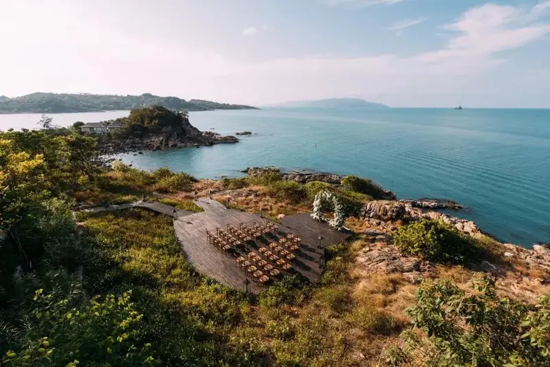 Terrasse en bois aménagée avec des tables et des chaises surplombe une côte rocheuse et la mer.
