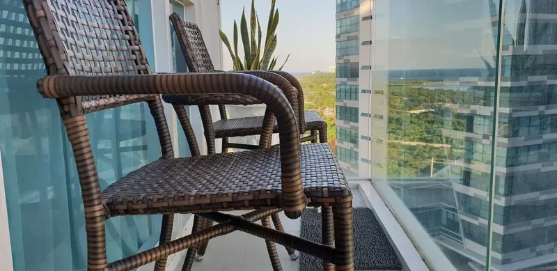 Trois fauteuils en osier sur un balcon avec vue sur la ville et la mer.
