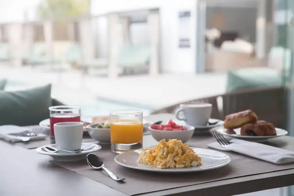 Une table est dressée avec un petit-déjeuner composé de boissons, de fruits et d'œufs brouillés.