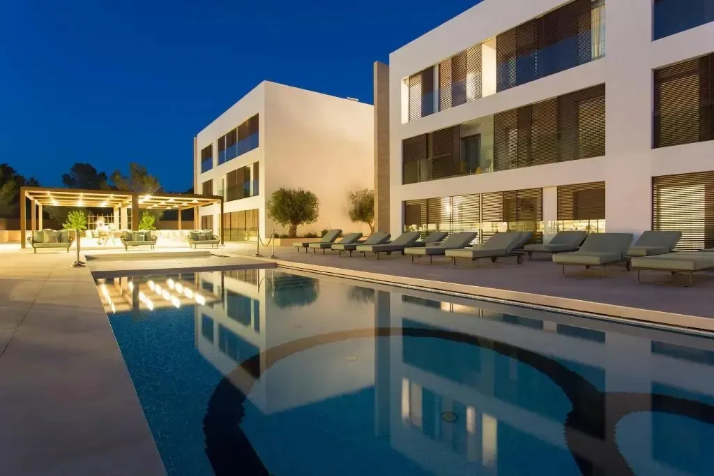 Piscine illuminée au crépuscule devant un bâtiment moderne.
