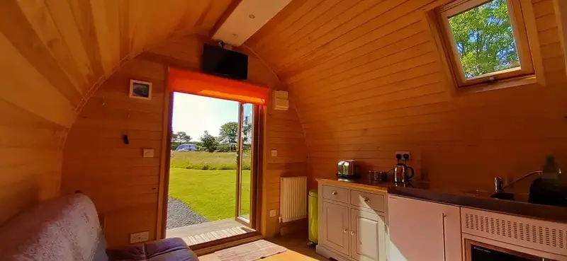 Intérieur chaleureux d'un logement avec une kitchenette et une vue sur un jardin verdoyant.