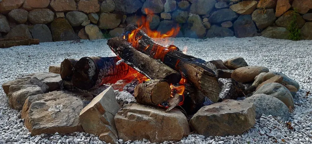 Un feu de bois crépite au centre d'un espace gravillonné, entouré de pierres.