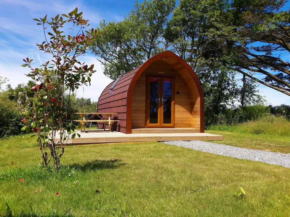 Une cabane en bois sur une pelouse verdoyante, avec une table et des bancs en bois devant.