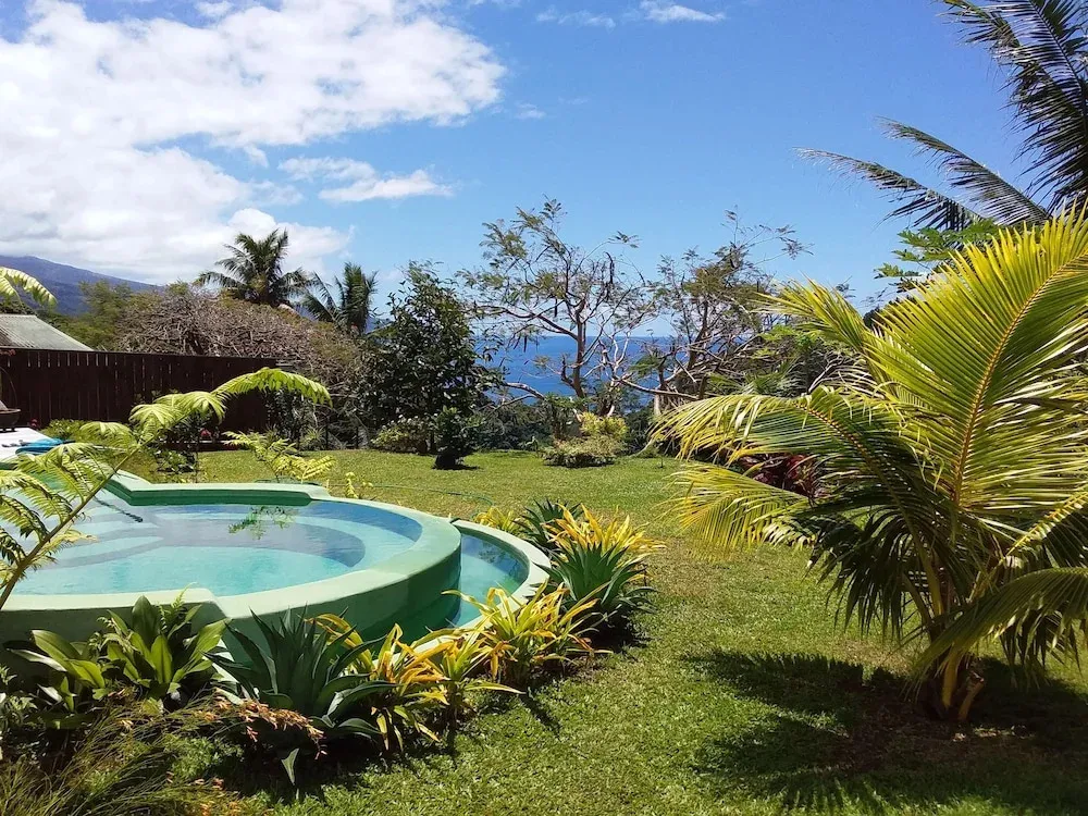 Une piscine turquoise s'intègre dans un jardin tropical verdoyant avec vue sur la mer.