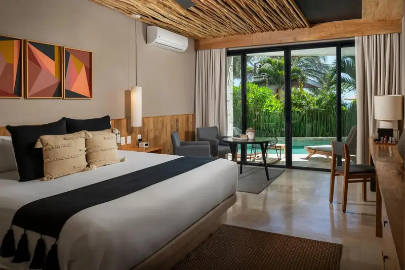 Une chambre lumineuse avec un grand lit et un coin salon donnant sur une piscine.