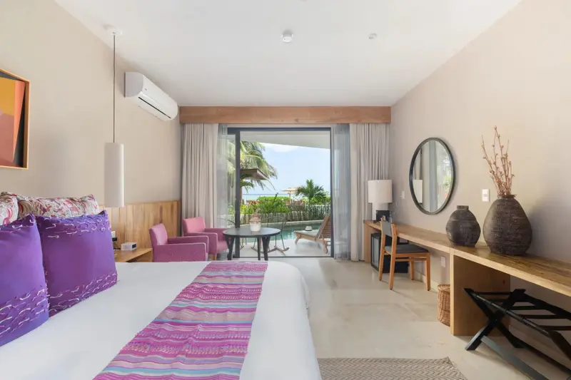 Chambre lumineuse avec un grand lit et vue sur une piscine et la mer.
