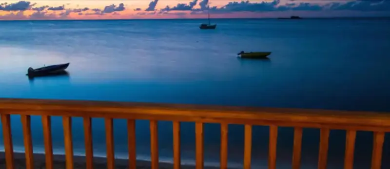 Vue sur la mer calme au coucher du soleil depuis une balustrade en bois.