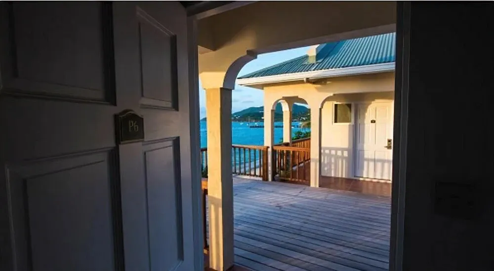 Une porte ouverte donne sur une terrasse en bois avec vue sur la mer.