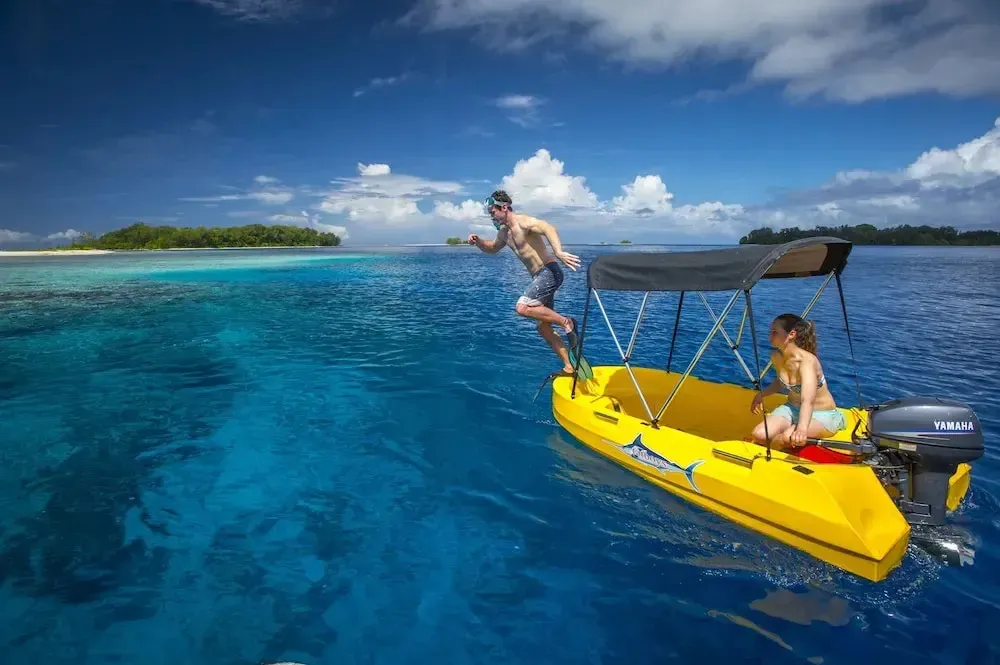 Une personne saute d'un bateau jaune dans une eau turquoise.