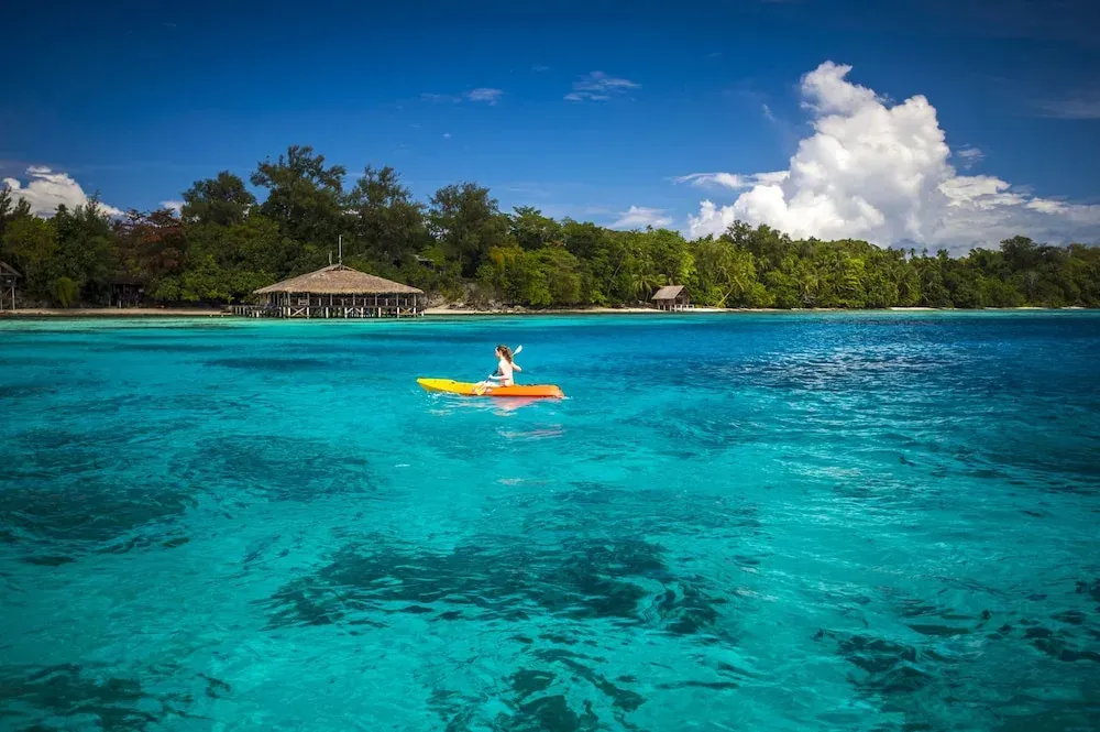 Une personne pratique le kayak sur une eau turquoise et claire.