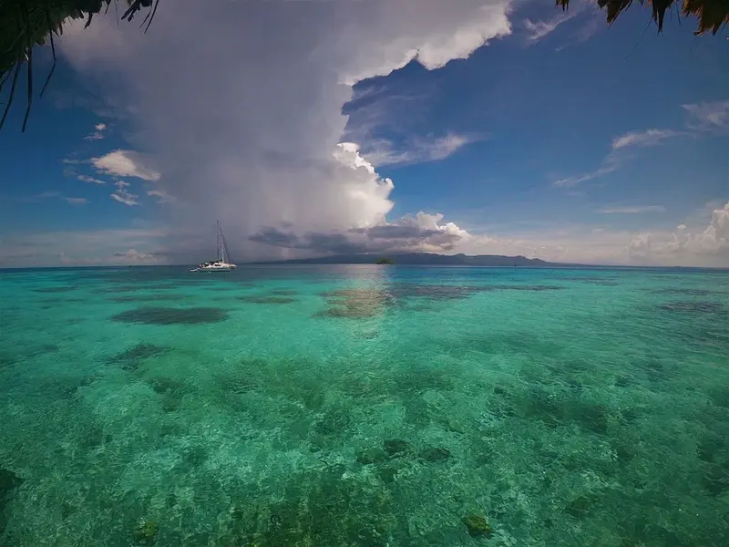 Vaste étendue d'eau turquoise sous un ciel nuageux avec un voilier à l'horizon.