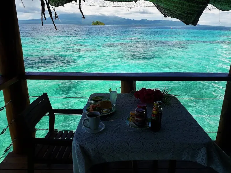 Une table est dressée avec un petit-déjeuner face à une mer turquoise.