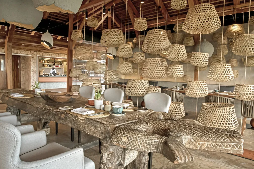 Une longue table en bois massif est dressée dans une salle à manger décorée de luminaires en osier.