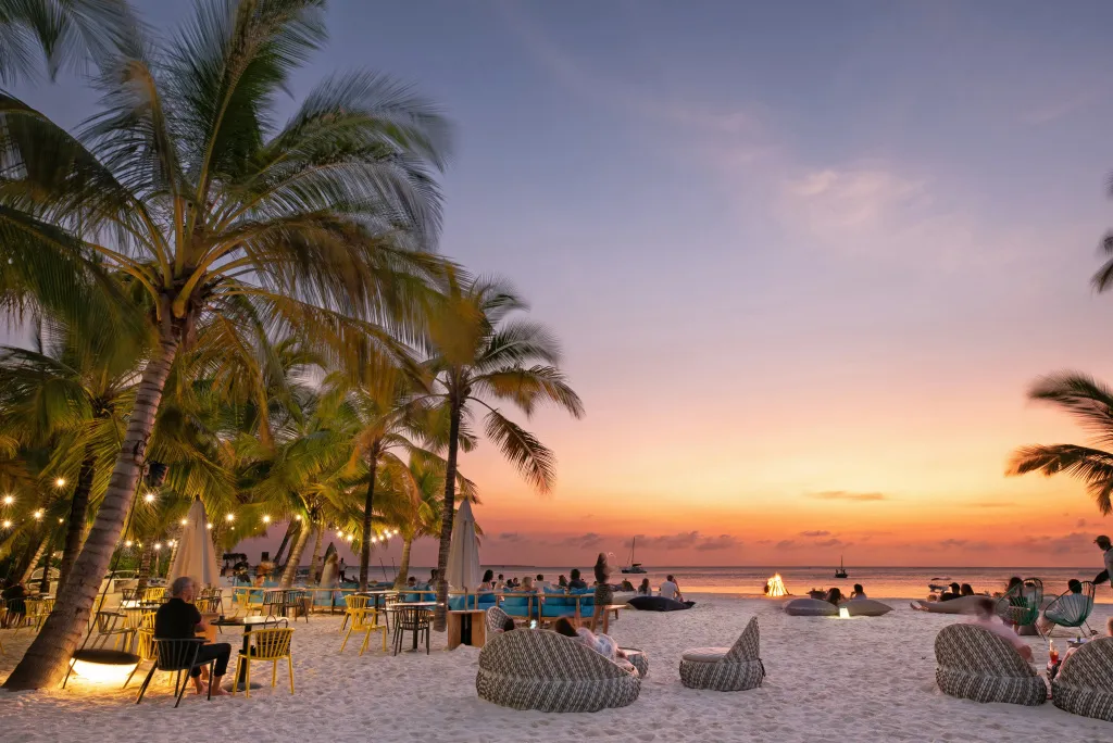 Des convives se détendent sur une plage au coucher du soleil.