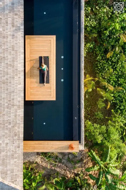 Une personne se détend sur une plateforme en bois au centre d'une piscine rectangulaire.