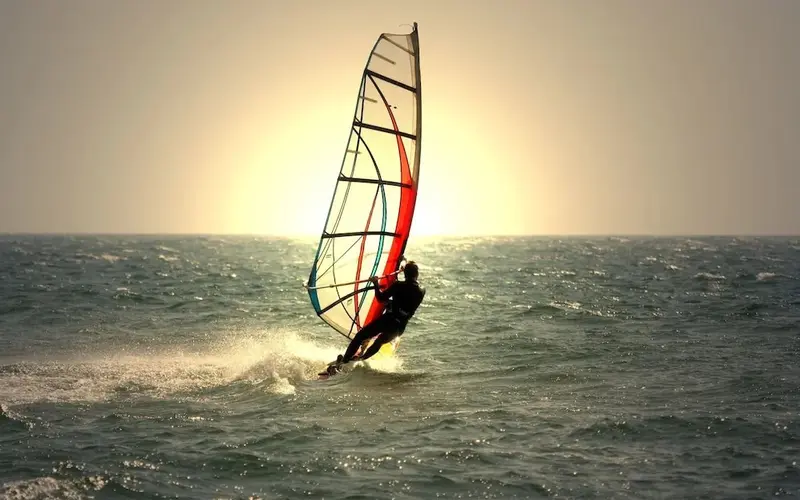Un pratiquant de planche à voile s'envole au-dessus des vagues au coucher du soleil.