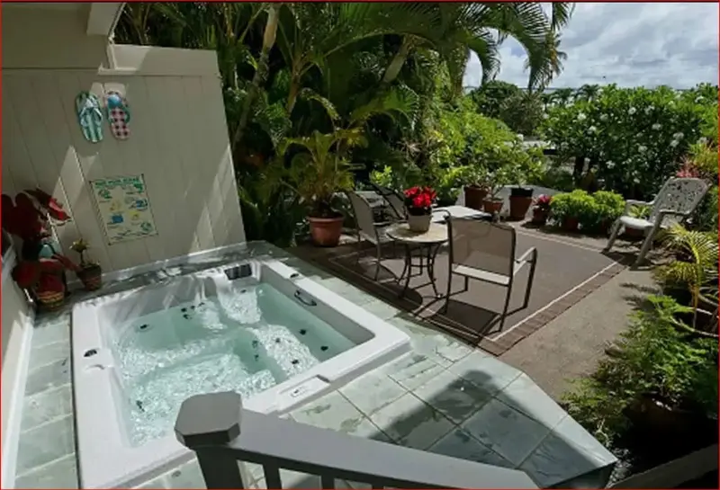 Un jacuzzi extérieur est entouré de végétation luxuriante et de mobilier de jardin.