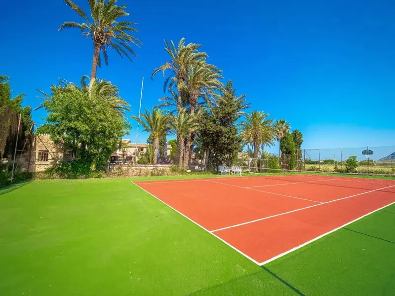 Terrain de tennis en terre battue entouré de végétation luxuriante sous un ciel bleu.