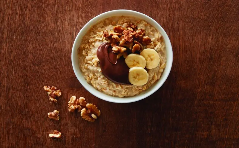 Un bol de porridge aux noix et aux bananes est présenté sur une surface en bois.